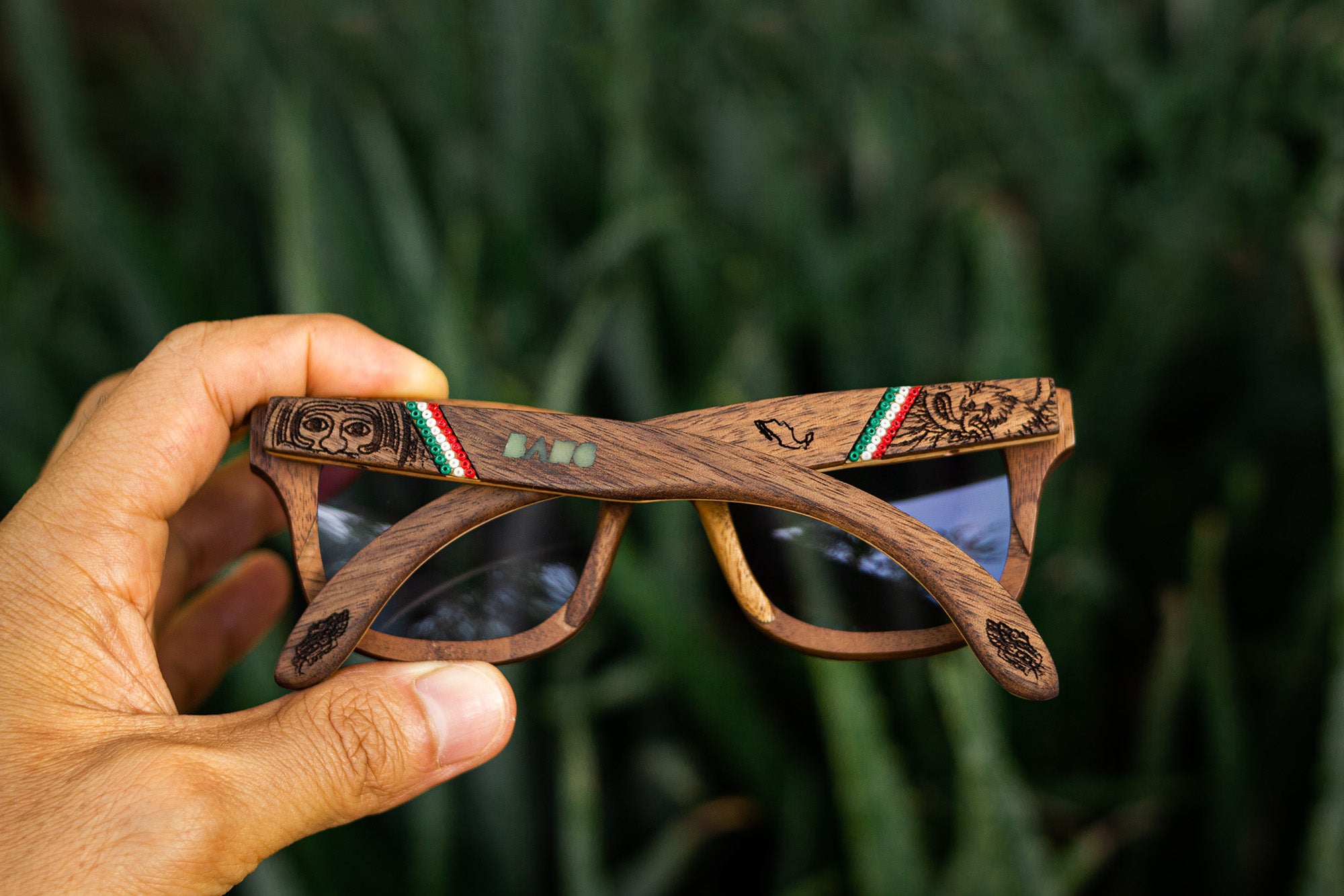 Mano sosteniendo unos lentes de madera Bang con grabado referente a México y artesanía huichol