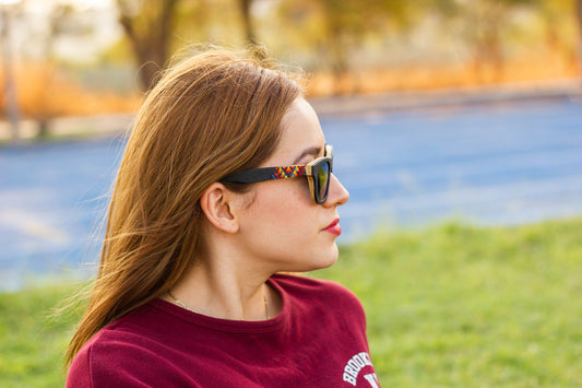 Modelo mujer con lentes wixarika de sol Bang, Fuego Ébano Negro, lentes oscuros, micas negras polarizadas, atardecer en una cancha con pista de atletismo