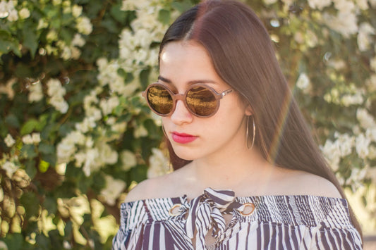 Modelo mujer con lentes de madera redondos, marca bang, modelo kiin, micas cafés, modernos, fondo con naturaleza