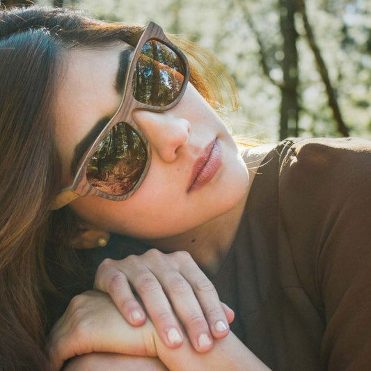 Modelo mujer usando lentes de madera palisandro, marca bang, fondo de naturaleza bokeh