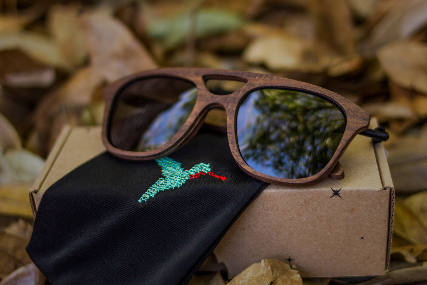 Lentes de madera Bang, cobá mica humo, sobre caja de cartón y morral bordado en punto de cruz con colibrí