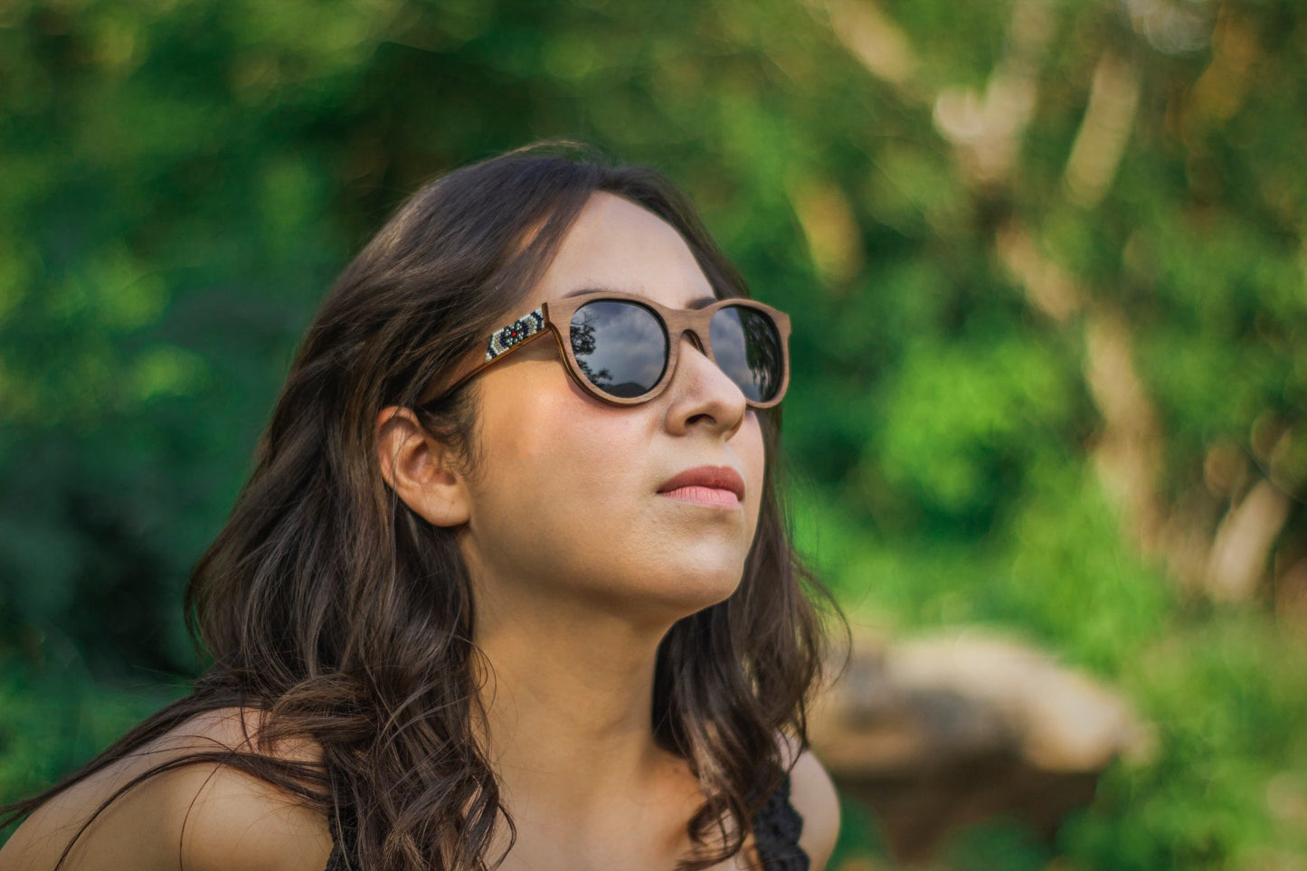 Modelo mujer con lentes huicholes hikuri plata, marca Bang, intervenidos con artesanía huichol, fondo naturaleza bokeh