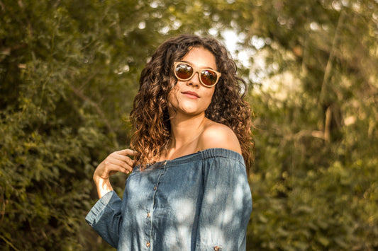 Modelo mujer con lentes polarizados de madera, marca bang, micas cafés, fondo de naturaleza con bokeh