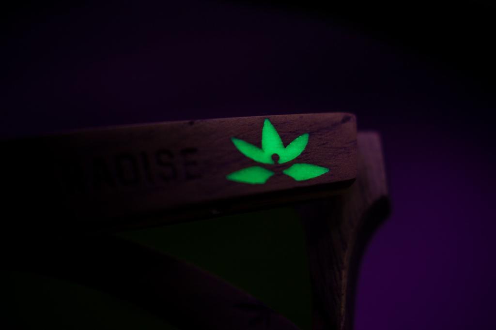 Detalle de logo de lentes paradise de bang brillando, se carga con luz solar, luz uv, fondo oscuro
