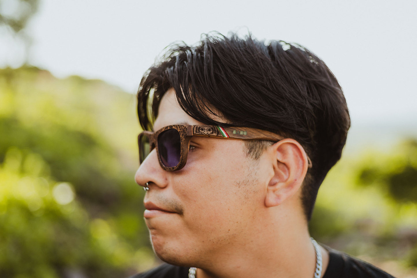 Modelo hombre usando unos lentes de madera huicholes, con grabado de calendario azteca, modelo mexa conmemorativo de México, fondo de naturaleza
