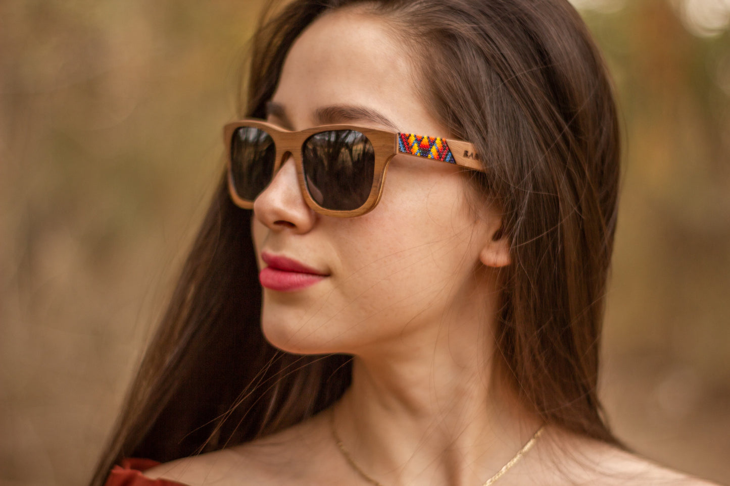 Modelo mujer, para ella, con lentes huicholes, marca bang, fabricados en madera, modelo fuego, artesanía de chaquira, fondo de naturaleza con bokeh
