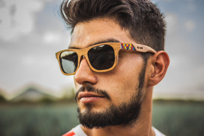 Modelo hombre, para él, con lentes huicholes, marca bang, fabricados en madera, modelo fuego, artesanía de chaquira, fondo de naturaleza con bokeh